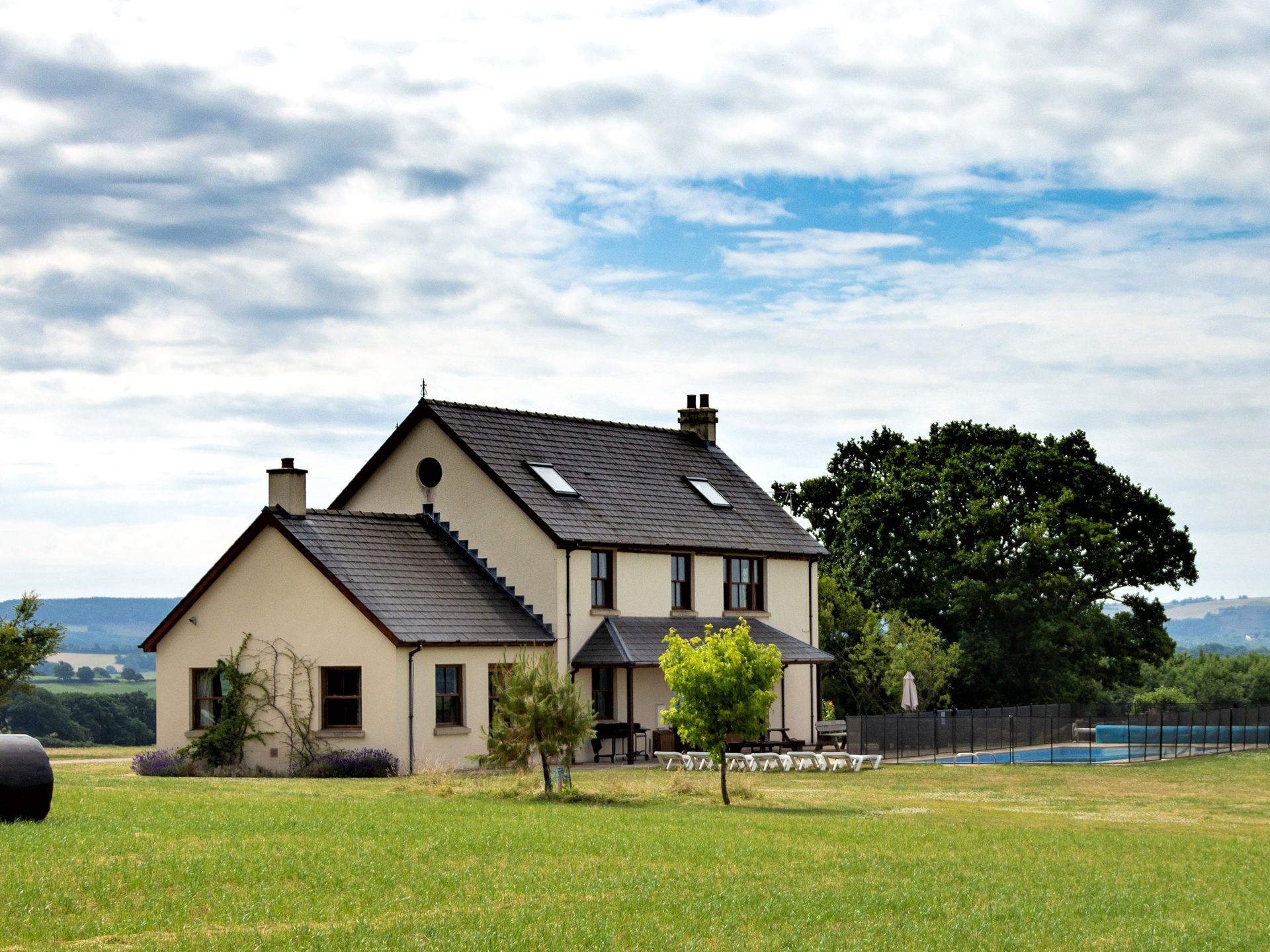 Modern cream cottage with grey slate roof set in pastoral countryside with views and swimming pool