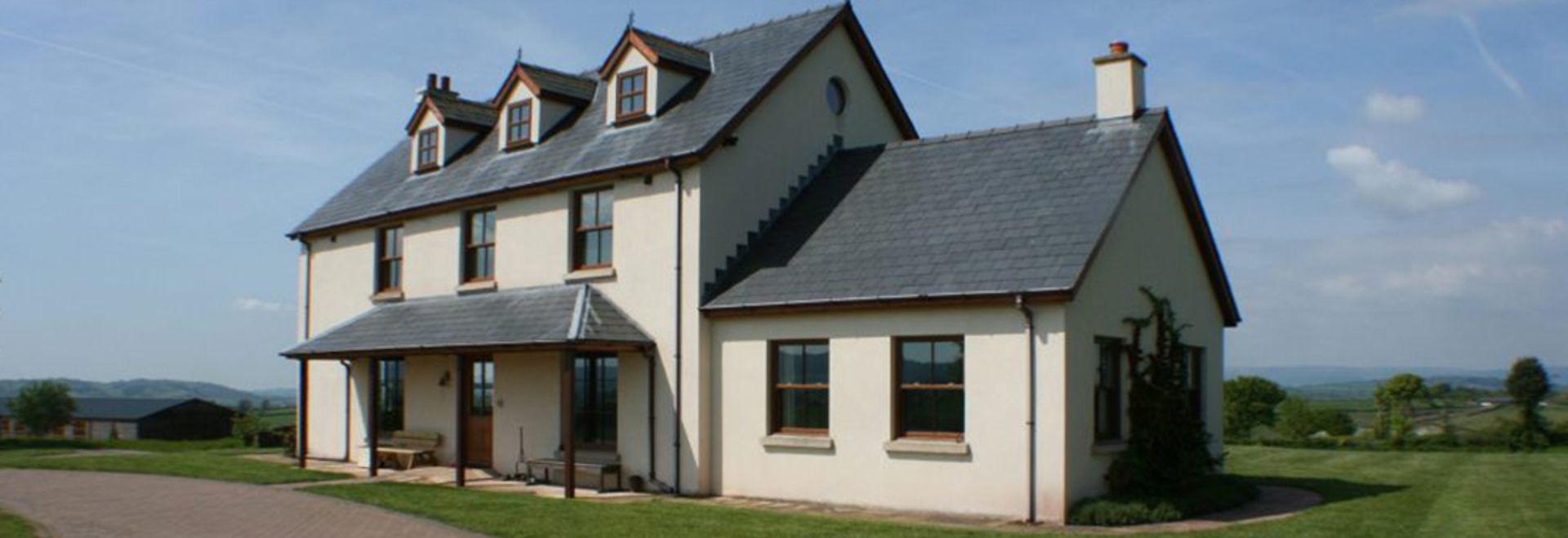 Two-storey cream and grey country house with dormer windows overlooking countryside landscape